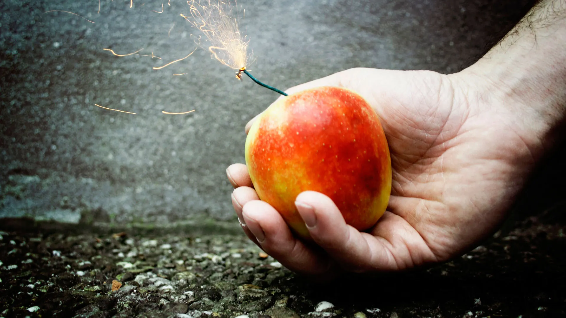 Eine Hand hält einen roten Apfel mit brennender Zündschnur